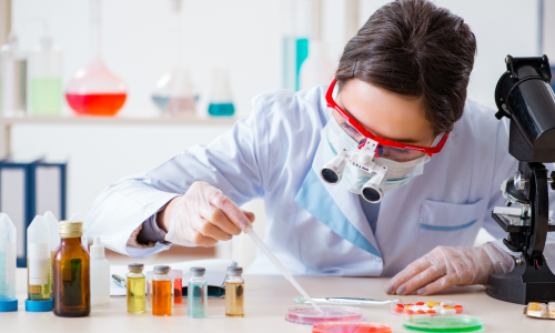 Naukowiec w odzieży ochronnej pracujący w laboratorium nad nowymi substancjami, symbolizujący złożony i długotrwały proces badań klinicznych leku.